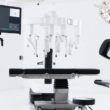Modern surgical suite with advanced robotic equipment, featuring multiple articulated arms and computer screens, creating a sleek, high-tech atmosphere.