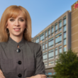 UMC new CEO Maria Zampini, confidently stands in front of a modern office building against a clear blue sky, conveying professionalism.