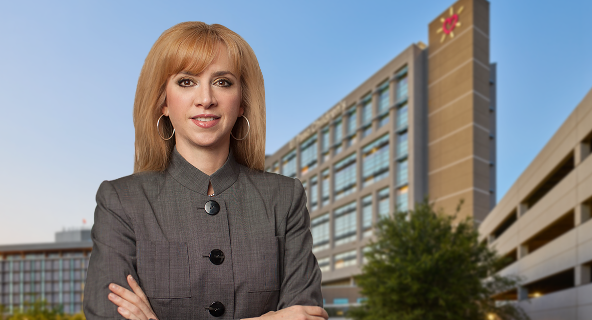 UMC new CEO Maria Zampini, confidently stands in front of a modern office building against a clear blue sky, conveying professionalism.