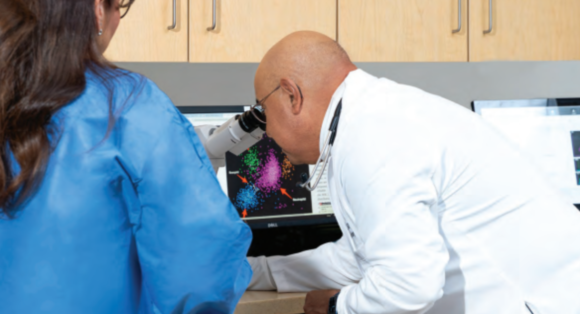 Dr. Jesus Gomez, a board-certified medical hematologist and oncologist examines colorful data via a microscope on a computer screen.