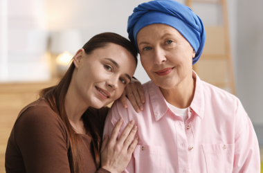 A loving portrait of two women; one with a blue headscarf, the other resting her head on her shoulder. They are indoors, representing National Cancer Survivors Day.