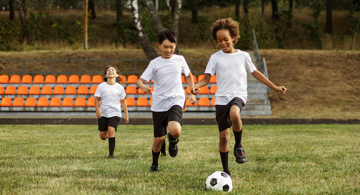 Three young boys are actively playing soccer on a grassy field, showcasing teamwork and enthusiasm.