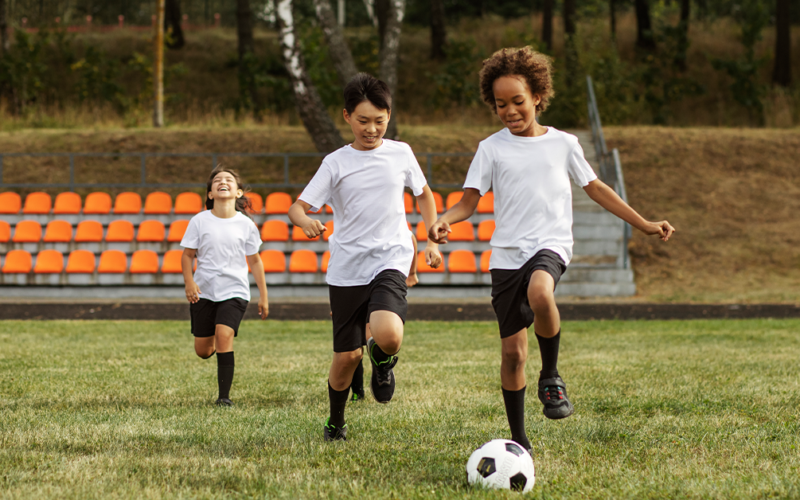 Three young boys are actively playing soccer on a grassy field, showcasing teamwork and enthusiasm.