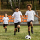 Three young boys are actively playing soccer on a grassy field, showcasing teamwork and enthusiasm.