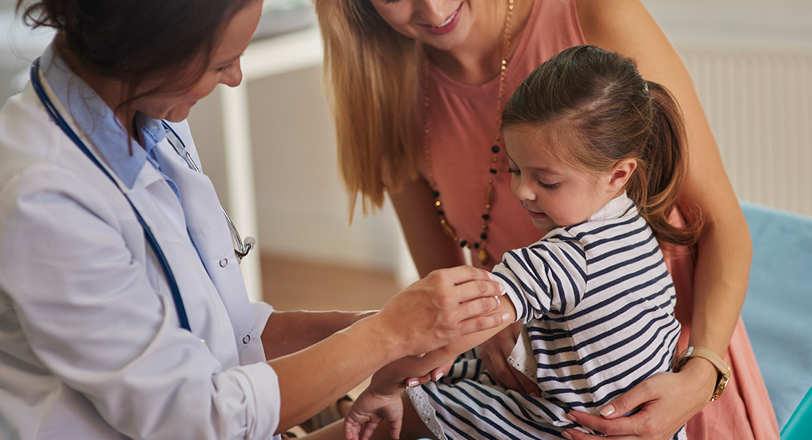 Healthcare provider prepares to vaccinate a young child while a parent offers support.