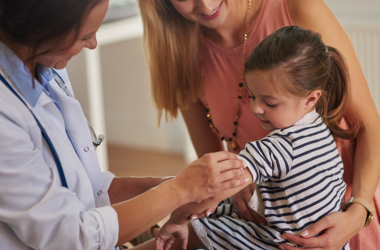 Healthcare provider prepares to vaccinate a young child while a parent offers support.