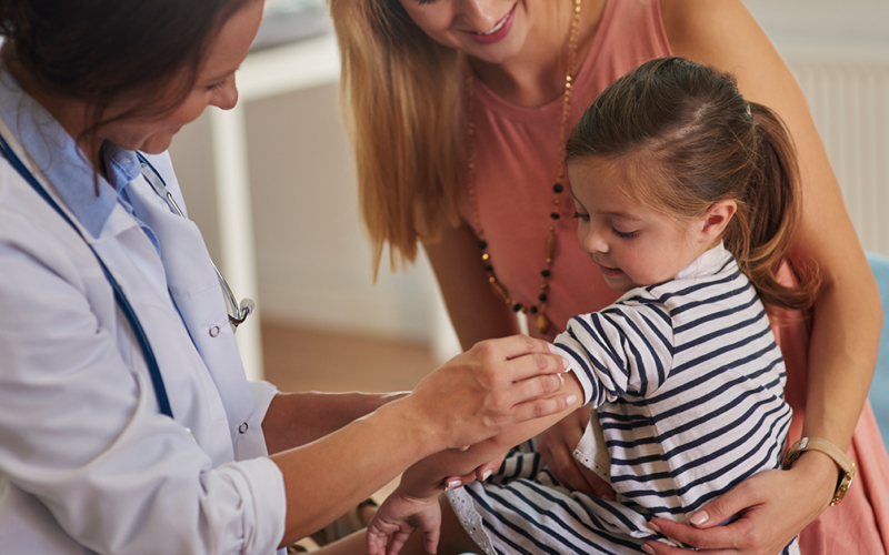 Healthcare provider prepares to vaccinate a young child while a parent offers support.