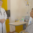 Dr. Philip E. Fiddler, Director of the UMC Burn Center, talks to Javier Diaz, a patient sitting in a hospital bed. The room has medical equipment.