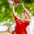 A joyful child reaches to catch a football, surrounded by trees in a park. The scene conveys excitement and playfulness on a sunny day.
