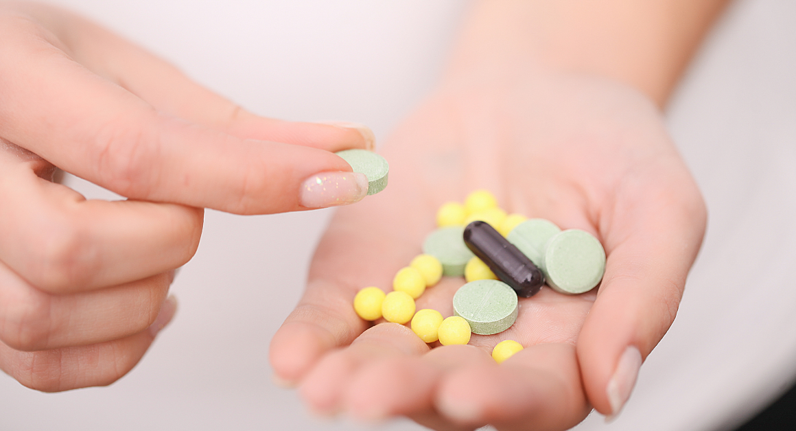 A hand holds various pills: green tablets, yellow round pills, and a black capsule. Another hand picks up a green tablet, conveying a clinical and focused tone.