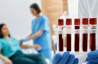 A healthcare professional holding a tray of blood samples in the foreground. In the background, a nurse prepares a patient for a blood draw, creating a clinical and focused atmosphere.