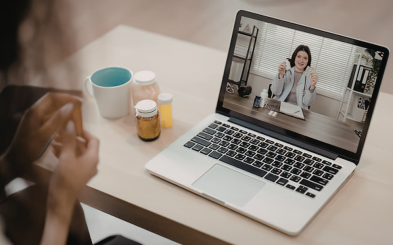 A sick patient having a telehealth call with a health professional over a computer.