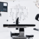 Modern surgical suite with advanced robotic equipment, featuring multiple articulated arms and computer screens, creating a sleek, high-tech atmosphere.