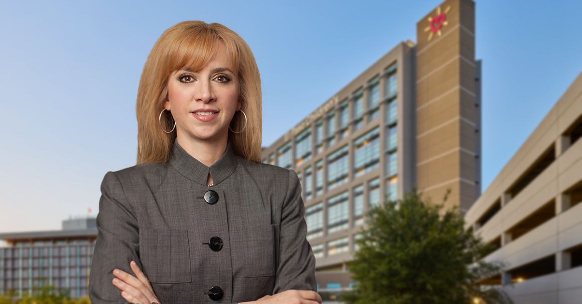 UMC new CEO Maria Zampini, confidently stands in front of a modern office building against a clear blue sky, conveying professionalism.