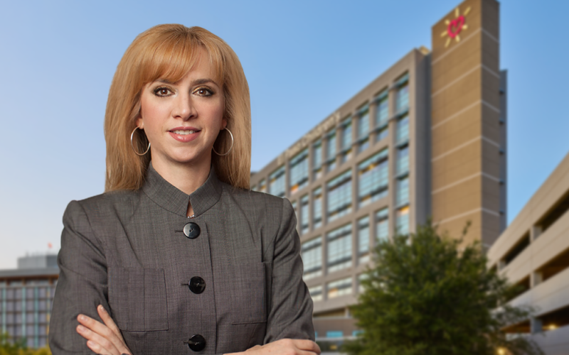 UMC new CEO Maria Zampini, confidently stands in front of a modern office building against a clear blue sky, conveying professionalism.