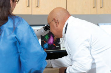 Dr. Jesus Gomez, a board-certified medical hematologist and oncologist examines colorful data via a microscope on a computer screen.