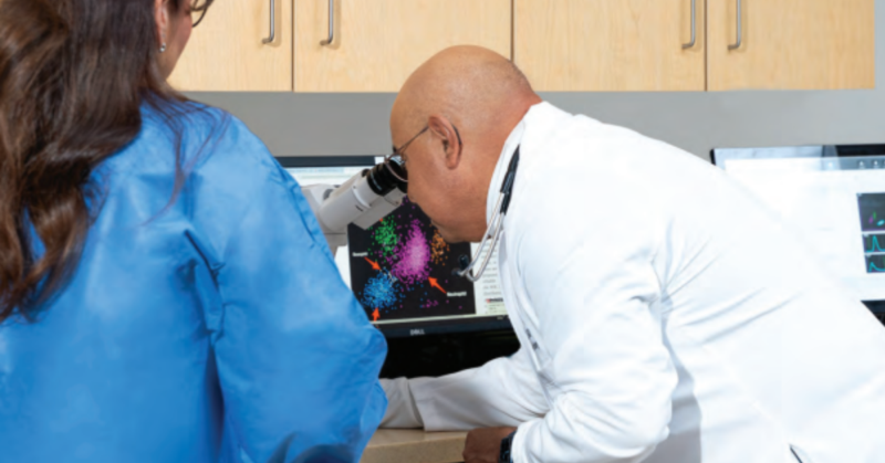 Dr. Jesus Gomez, a board-certified medical hematologist and oncologist examines colorful data via a microscope on a computer screen.