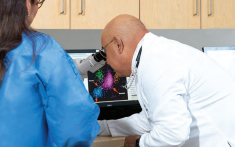 Dr. Jesus Gomez, a board-certified medical hematologist and oncologist examines colorful data via a microscope on a computer screen.
