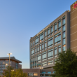 Modern hospital building with glass windows at dusk, labeled "El Paso Children's." Nearby, a tree and parking structure under a clear sky.