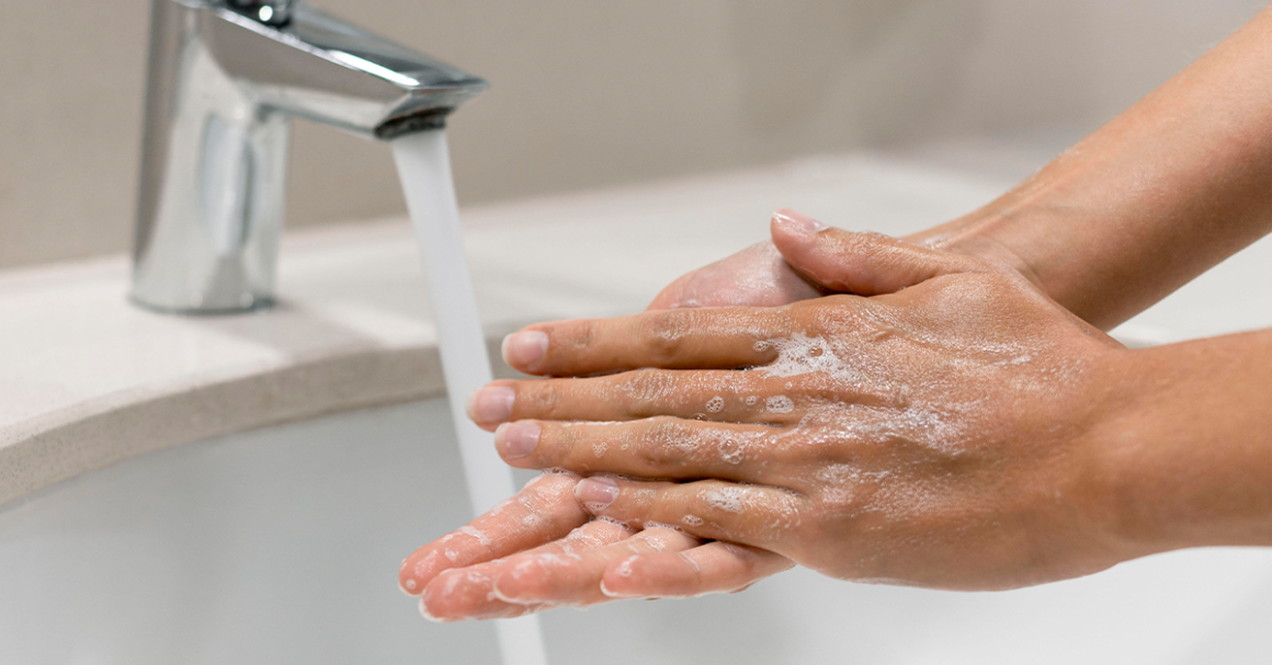 Two hands covered in soap under a running faucet, emphasizing cleanliness and hygiene.