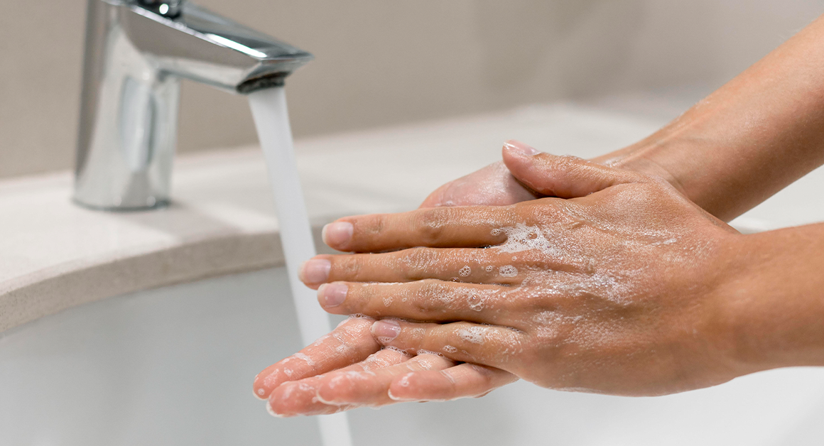 Two hands covered in soap under a running faucet, emphasizing cleanliness and hygiene.