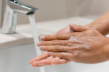 Two hands covered in soap under a running faucet, emphasizing cleanliness and hygiene.