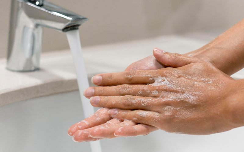 Two hands covered in soap under a running faucet, emphasizing cleanliness and hygiene.