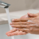 Two hands covered in soap under a running faucet, emphasizing cleanliness and hygiene.