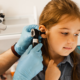 A healthcare professional examines a young girl's ear with an otoscope. The child looks calm and curious.