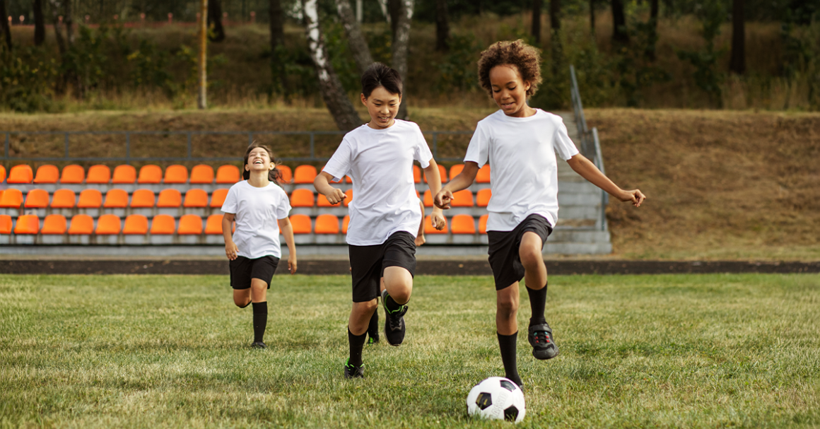 Three young boys are actively playing soccer on a grassy field, showcasing teamwork and enthusiasm.