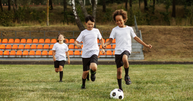 Three young boys are actively playing soccer on a grassy field, showcasing teamwork and enthusiasm.