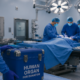Operating room with a surgical team performing an organ transplant as a staff member brings a cooler labeled "Human Organ for Donation."