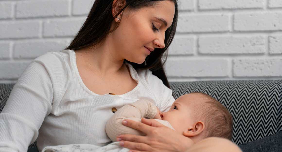 A woman breastfeeding an infant while sitting on a couch at home.