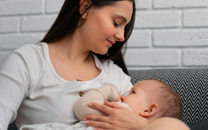 A woman breastfeeding an infant while sitting on a couch at home.