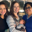 Three adults smile together while one holds a baby in a front carrier.