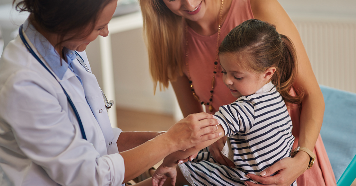 Healthcare provider prepares to vaccinate a young child while a parent offers support.