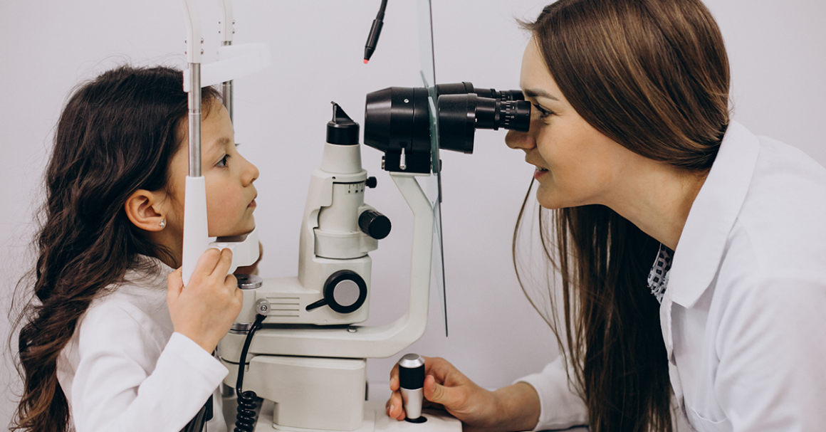 Eye doctor examines a young child's eyes using a slit lamp during an eye exam.