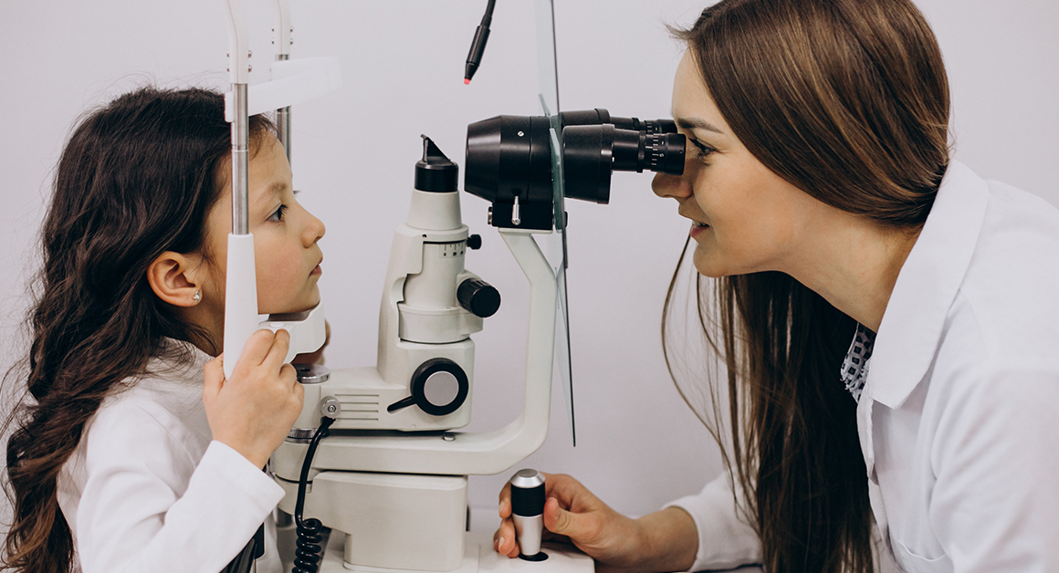 Eye doctor examines a young child's eyes using a slit lamp during an eye exam.