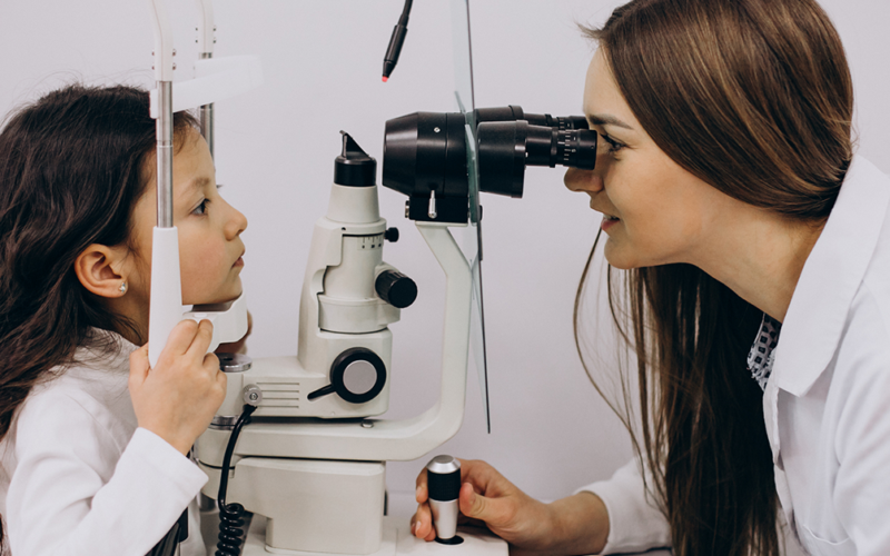 Eye doctor examines a young child's eyes using a slit lamp during an eye exam.