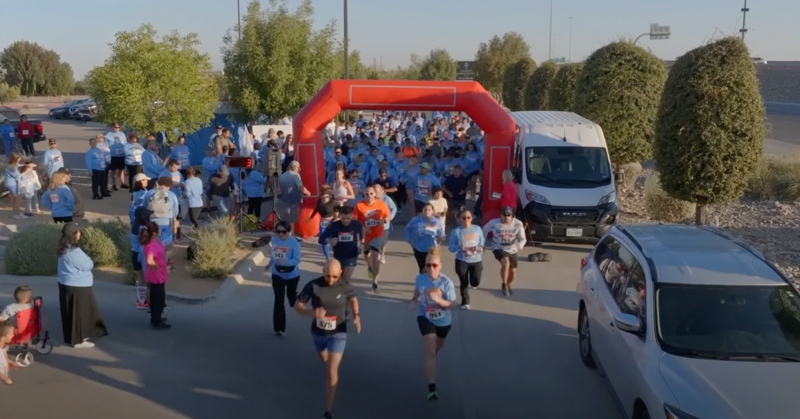 Participants run through the starting arch at the beginning of a community 5K race.