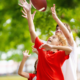 A joyful child reaches to catch a football, surrounded by trees in a park. The scene conveys excitement and playfulness on a sunny day.