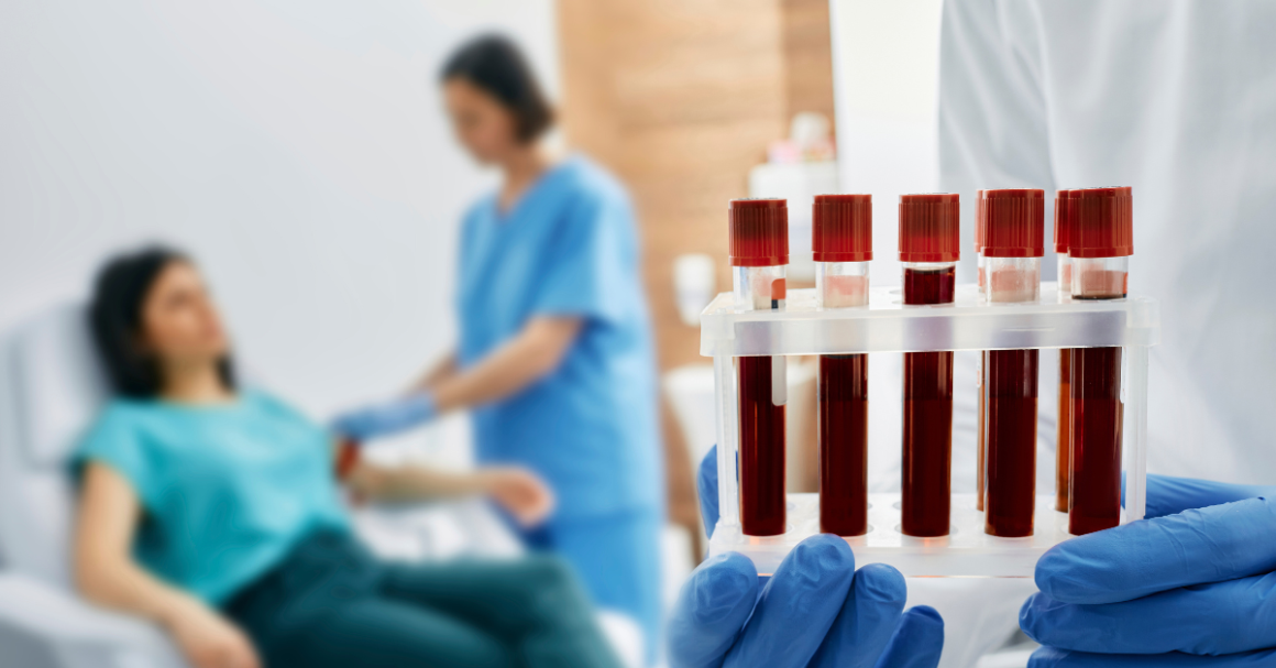 A healthcare professional holding a tray of blood samples in the foreground. In the background, a nurse prepares a patient for a blood draw, creating a clinical and focused atmosphere.