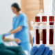 A healthcare professional holding a tray of blood samples in the foreground. In the background, a nurse prepares a patient for a blood draw, creating a clinical and focused atmosphere.