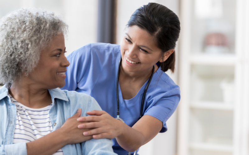 Nurse in blue scrubs smiling and offering reassurance to an older patient during a healthcare visit.