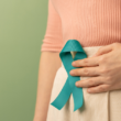 Person holding a teal awareness ribbon against their abdomen, representing ovarian cancer awareness and support.