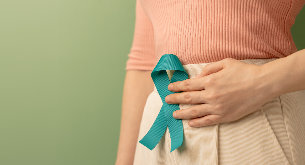 Person holding a teal awareness ribbon against their abdomen, representing ovarian cancer awareness and support.