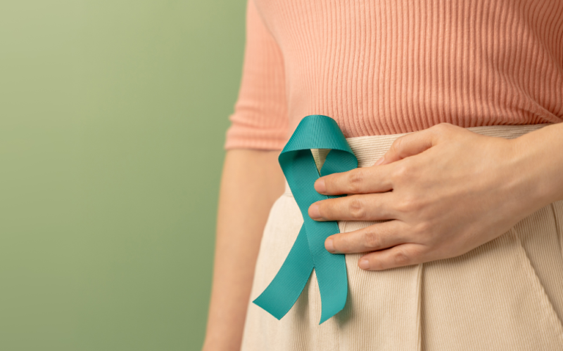 Person holding a teal awareness ribbon against their abdomen, representing ovarian cancer awareness and support.