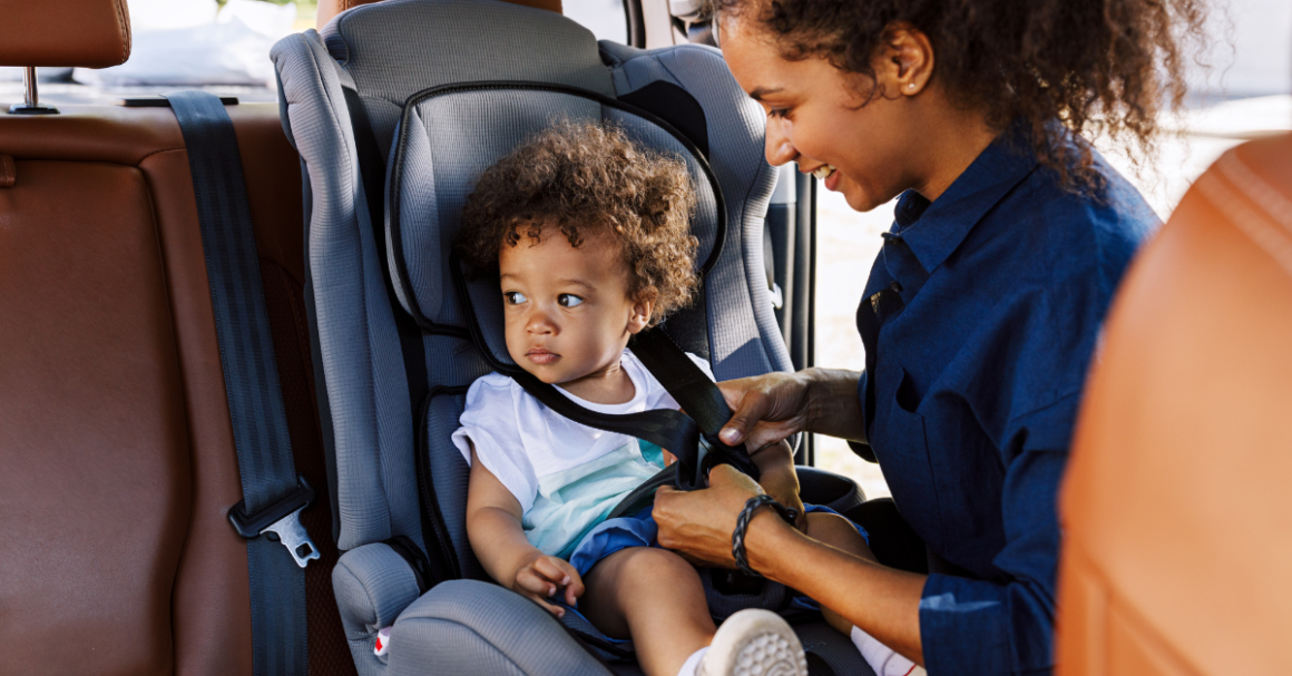 A mother secures her young child in a car seat before traveling.