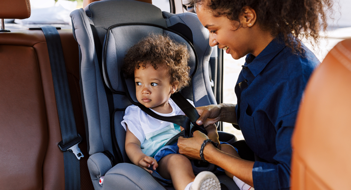 A mother secures her young child in a car seat before traveling.