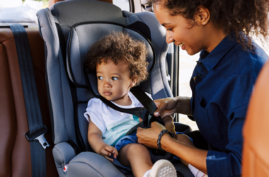 A mother secures her young child in a car seat before traveling.